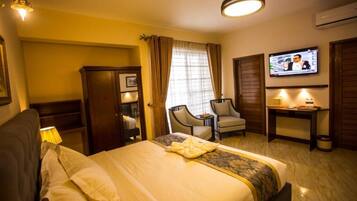 Una habitación de hotel con cama, escritorio, silla, televisor y armario.