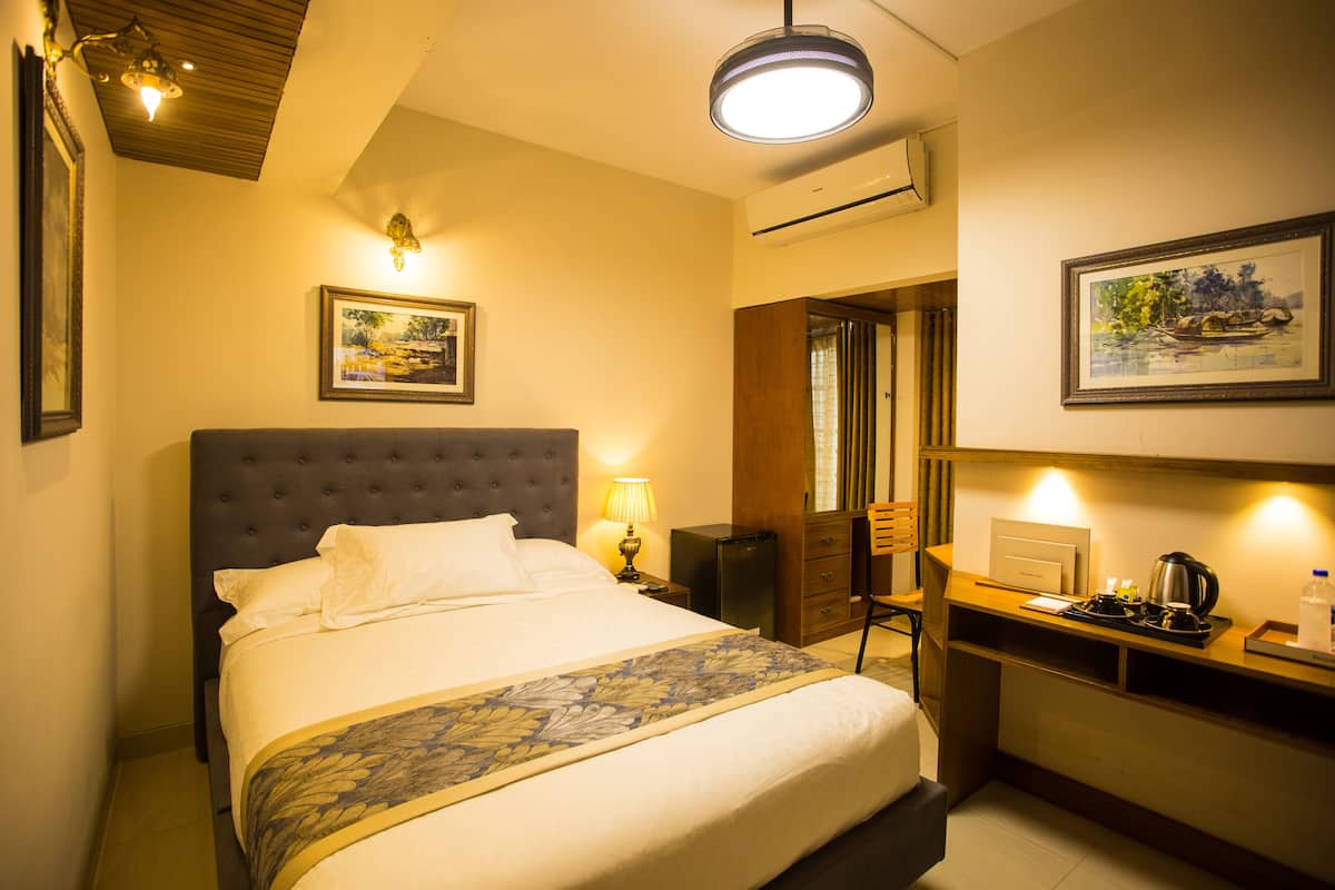 A hotel room with a bed, a desk, a chair, a lamp, and a painting on the wall.