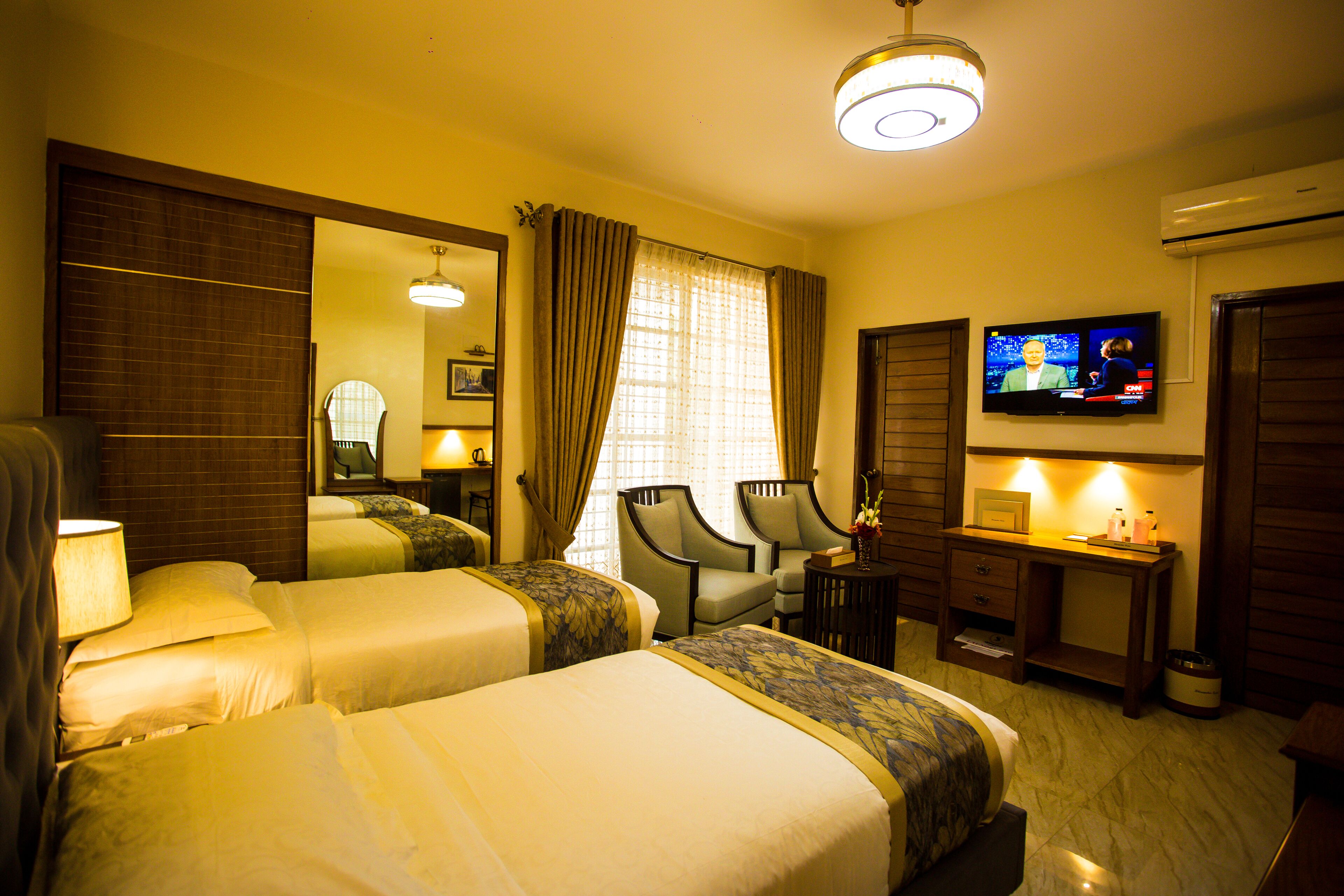 A hotel room with two beds, a desk, a chair, a television, and a mirror.