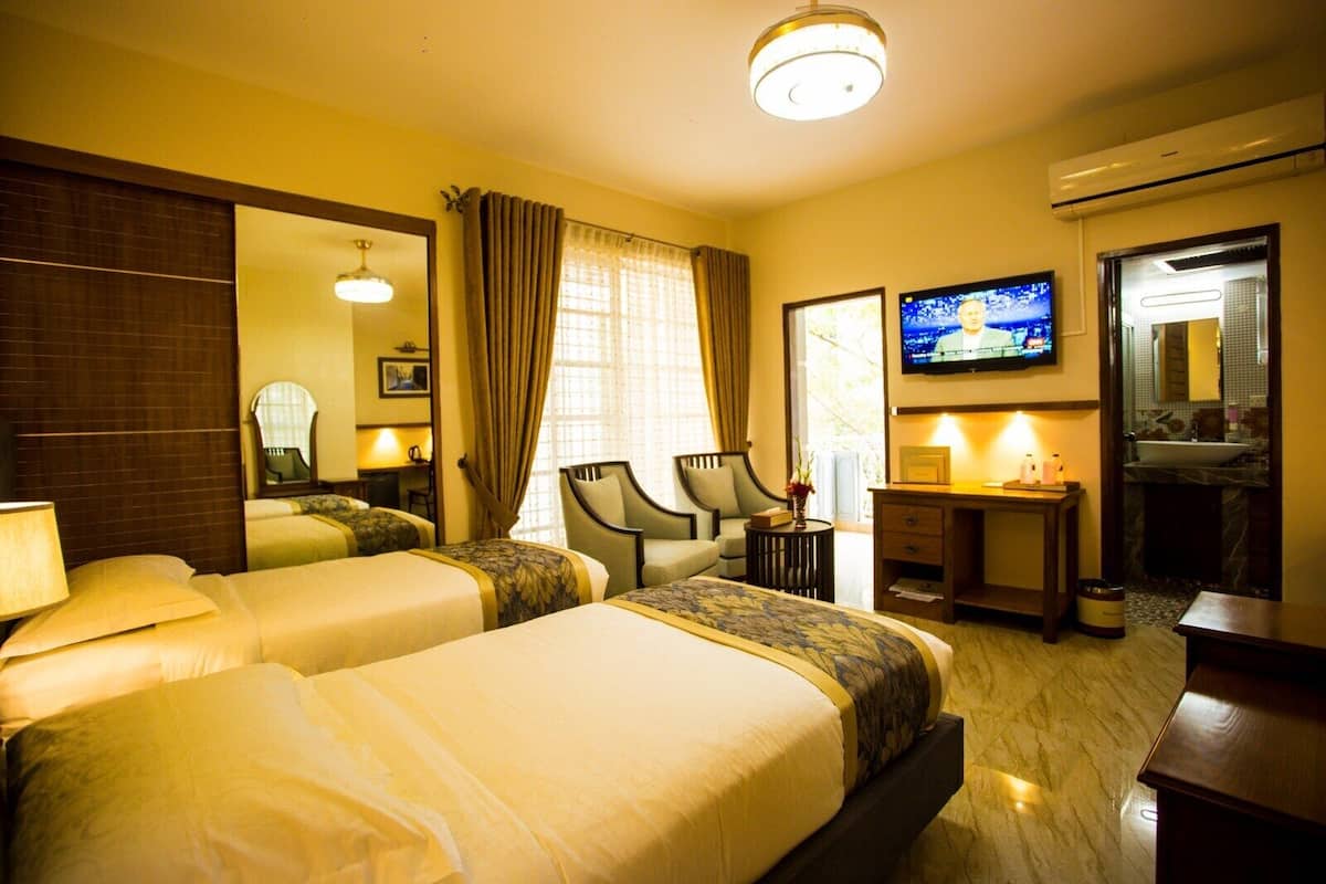 A hotel room with two beds, a TV, a desk, a chair, and a bathroom visible through an open door.