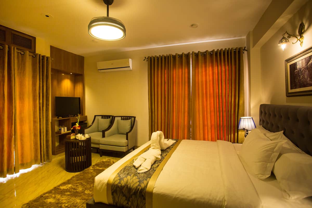A hotel room with a bed, a sofa, a TV, and an air conditioning unit.