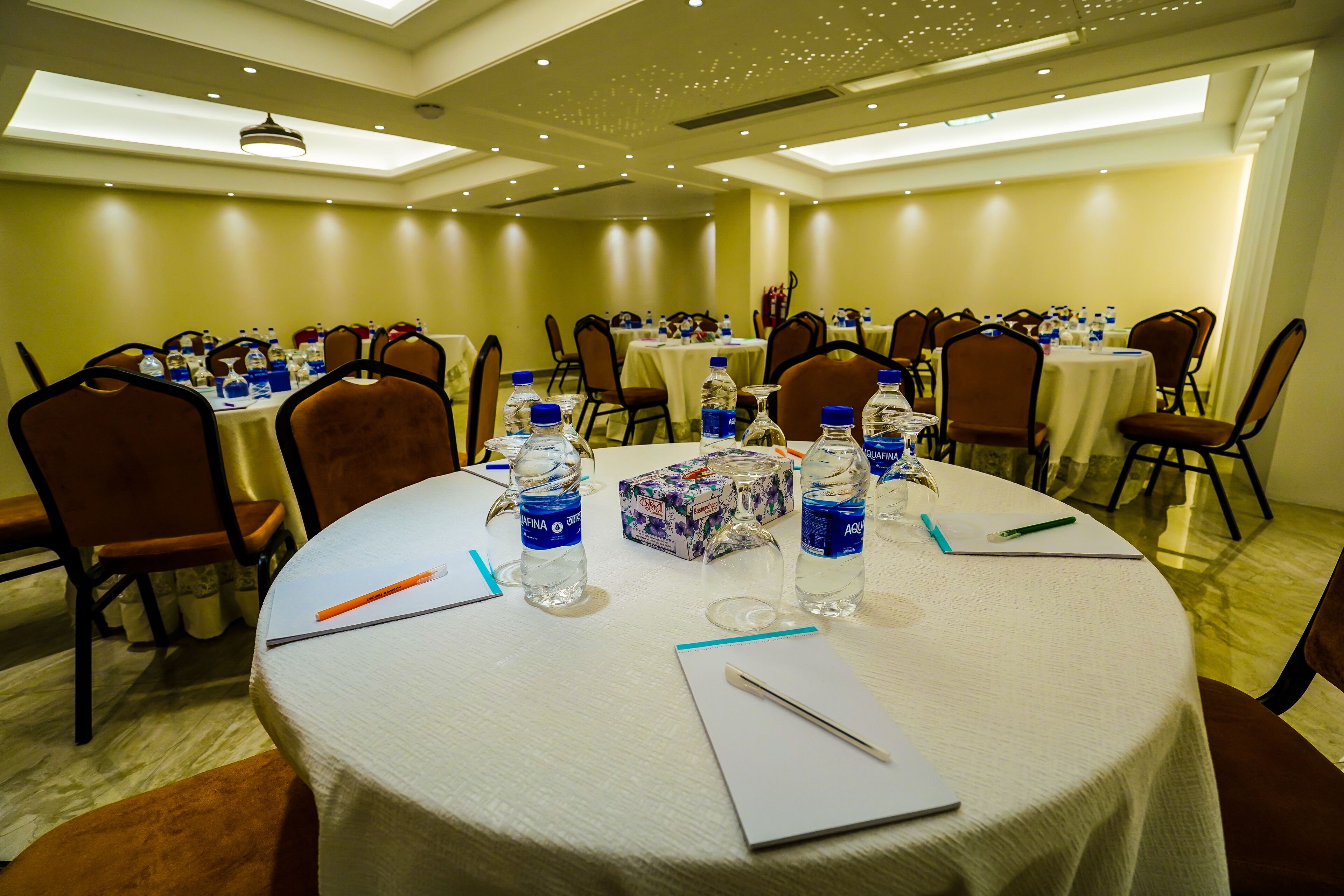 A conference room with round tables, chairs, water bottles, and a box of tissues.