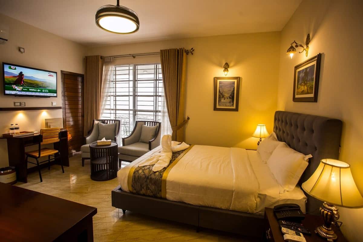 A hotel room with a bed, two armchairs, a desk, a TV, and a window with curtains.