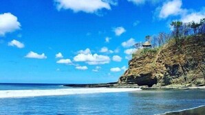 A beach with clear blue water, a sandy shore, and a rocky cliff with sparse vegetation. - Verdad Nicaragua Beach Hotel & Retreat (San Juan del Sur)