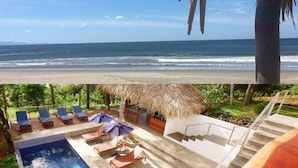 A pool area with lounge chairs and umbrellas, a thatched-roof structure, and a view of the ocean. - Verdad Nicaragua Beach Hotel & Retreat (San Juan del Sur)