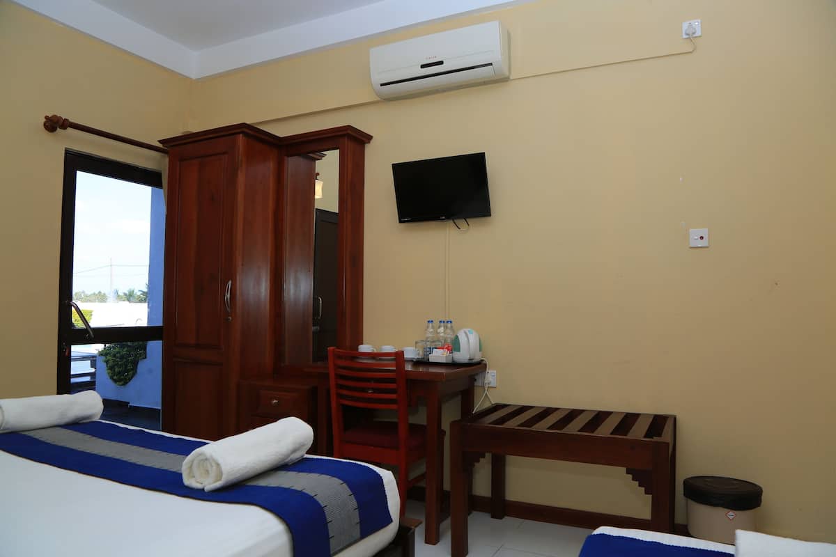 Een hotelkamer met een bed, een houten garderobe, een aan de muur bevestigde televisie, een klein tafeltje met een stoel, en een airconditioning.