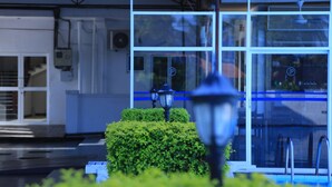 A modern building with a glass facade, a blue-lit entrance, and a small hedge in the foreground. - PJ Hotels Jaffna (Valikamam East)