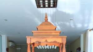 A wooden shrine with a seated deity, a small table with offerings, and a staircase in the background. - PJ Hotels Jaffna (Valikamam East)