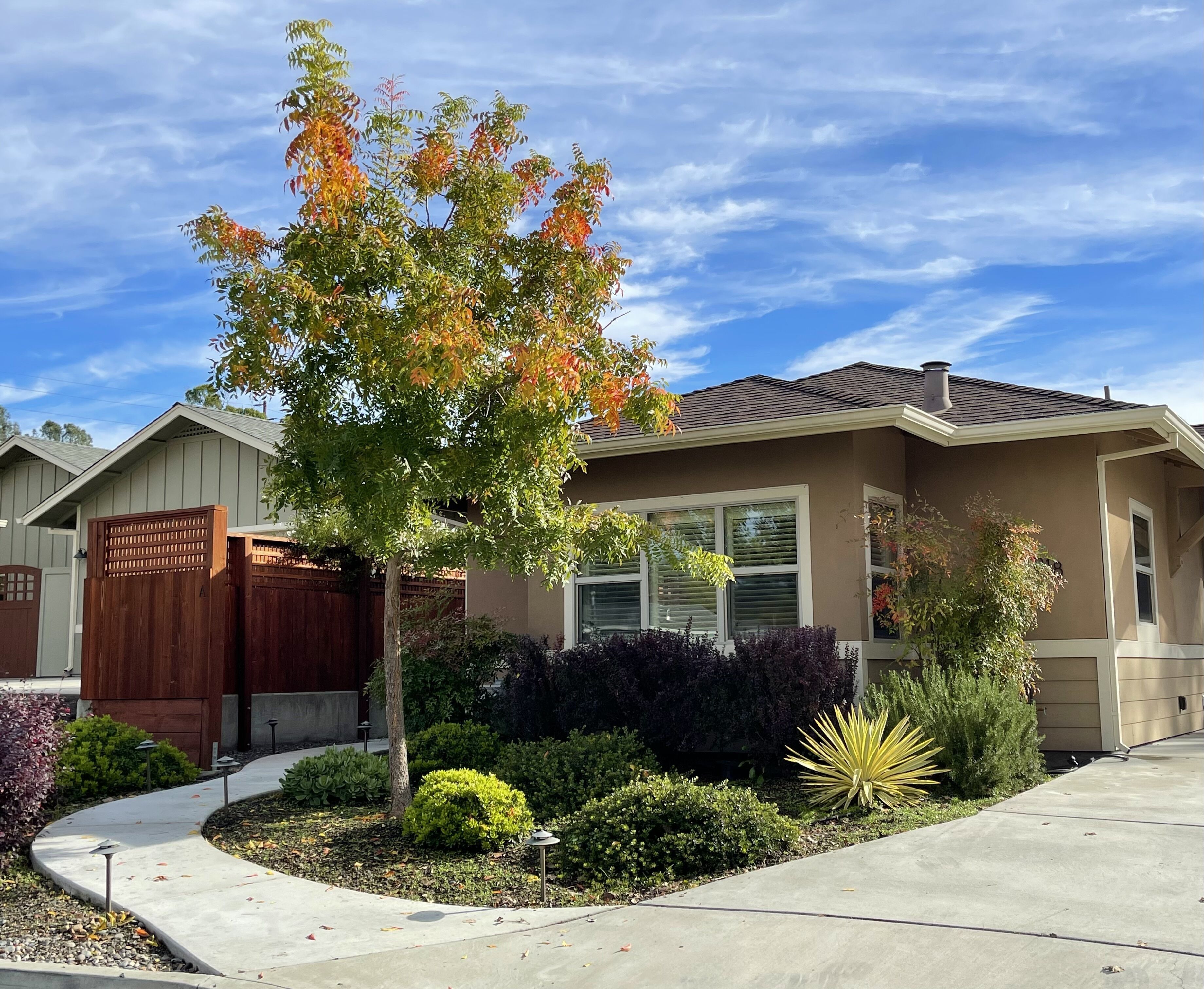 A residential house with a well-maintained garden, a wooden fence, and a clear sky.