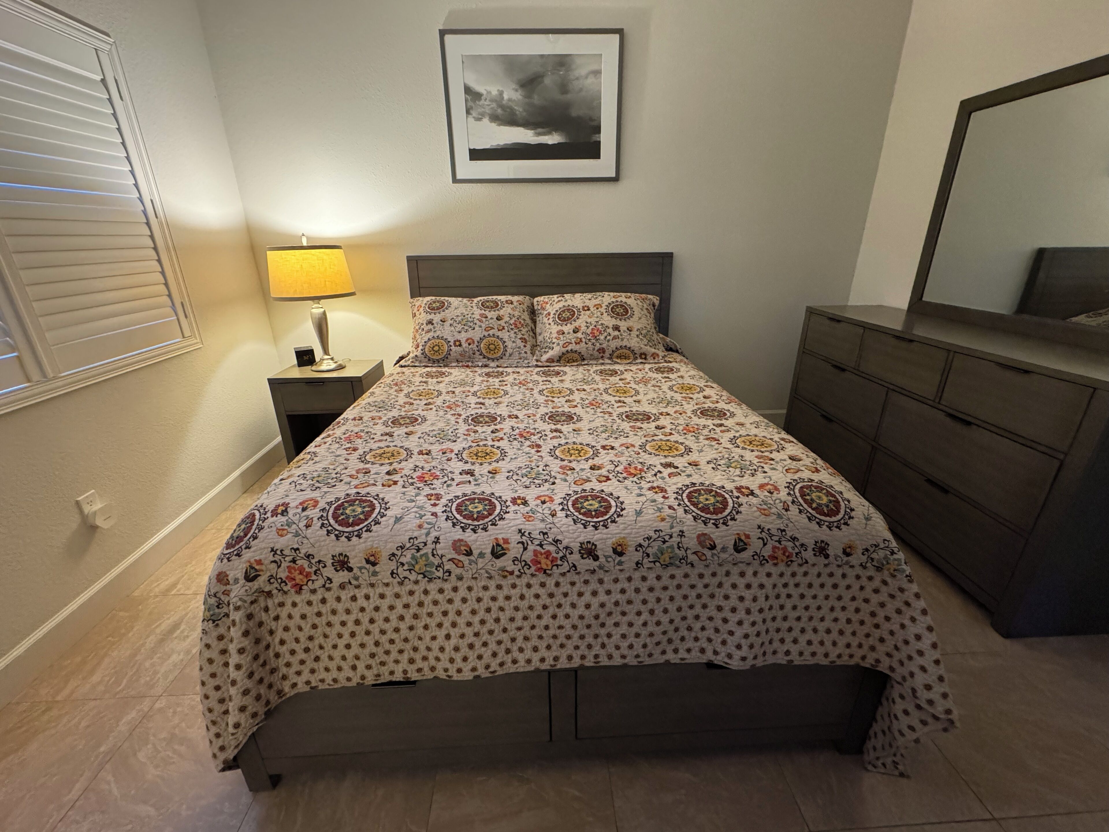 Quarto com cama, mesa de cabeceira, cômoda e um quadro na parede.