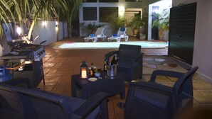 Um pátio externo com piscina, espreguiçadeiras e área de churrasco.