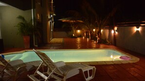 Piscina com espreguiçadeiras e área de estar à noite.