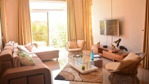Uma sala de estar moderna com um sofá, poltronas, uma mesa de centro de vidro e uma televisão de tela plana.