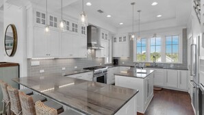 Une cuisine moderne avec des meubles blancs, un grand îlot central et des luminaires suspendus.
