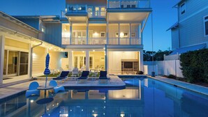 Une maison à plusieurs étages dotée d’une piscine, d’un espace salon extérieur et d’un balcon bien éclairé.