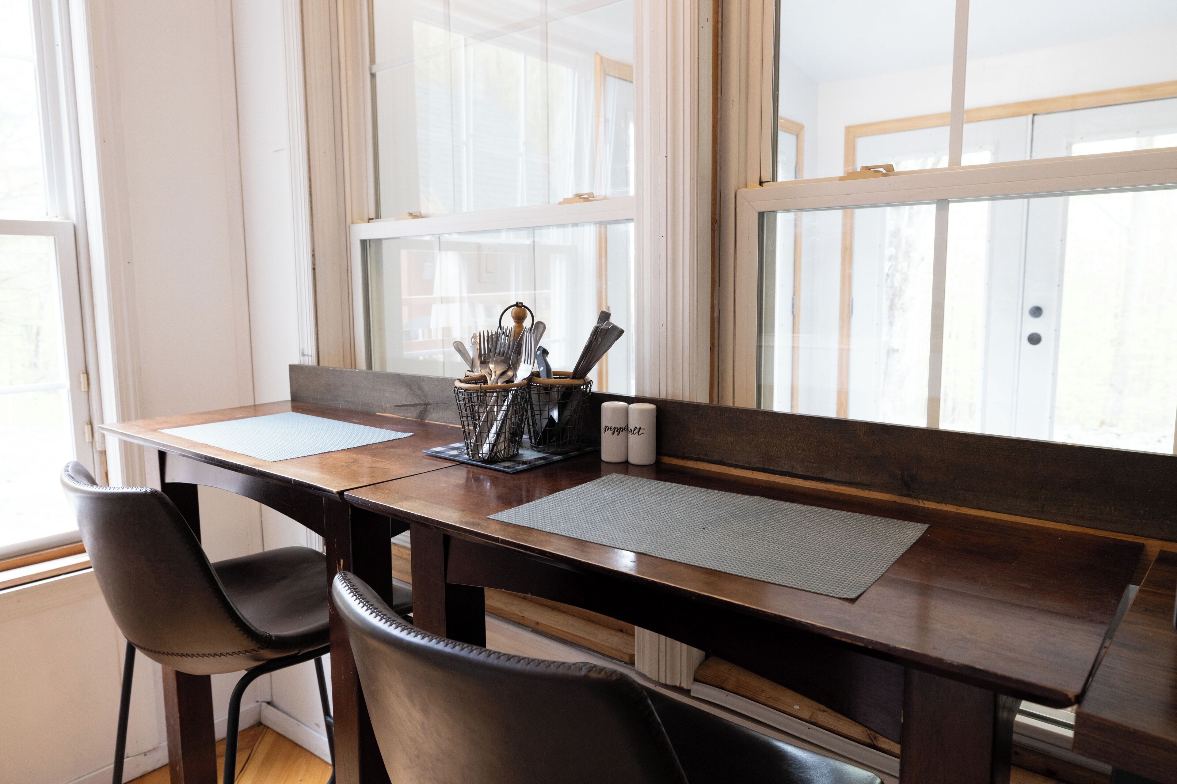 Een eethoek met een houten tafel, twee zwarte stoelen, een metalen bestekhouder en twee witte kandelaars.