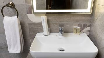 A bathroom with a white sink, a towel ring, and a mirror with a light above it.