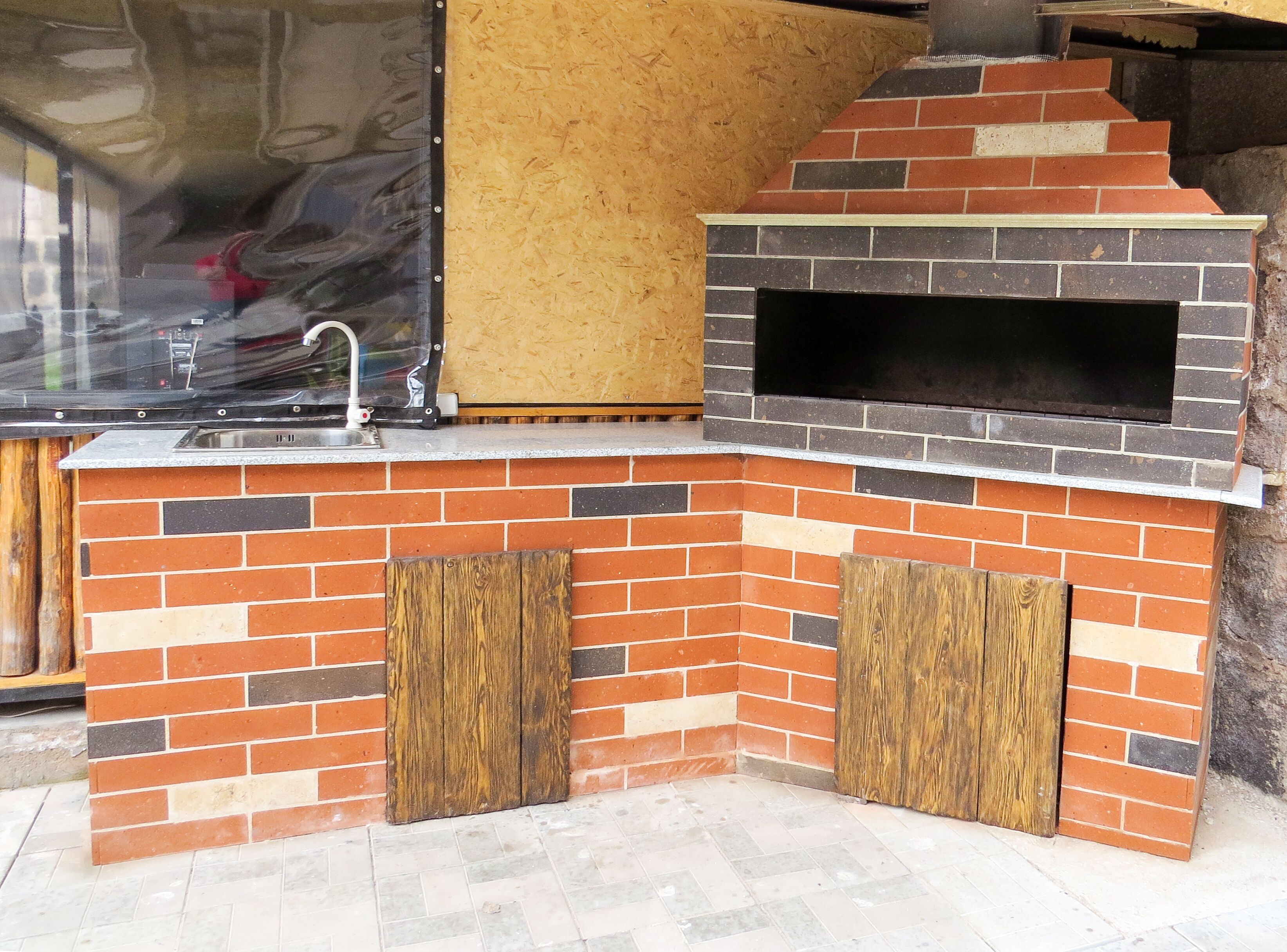 A brick-built outdoor kitchen with a sink and a pizza oven.