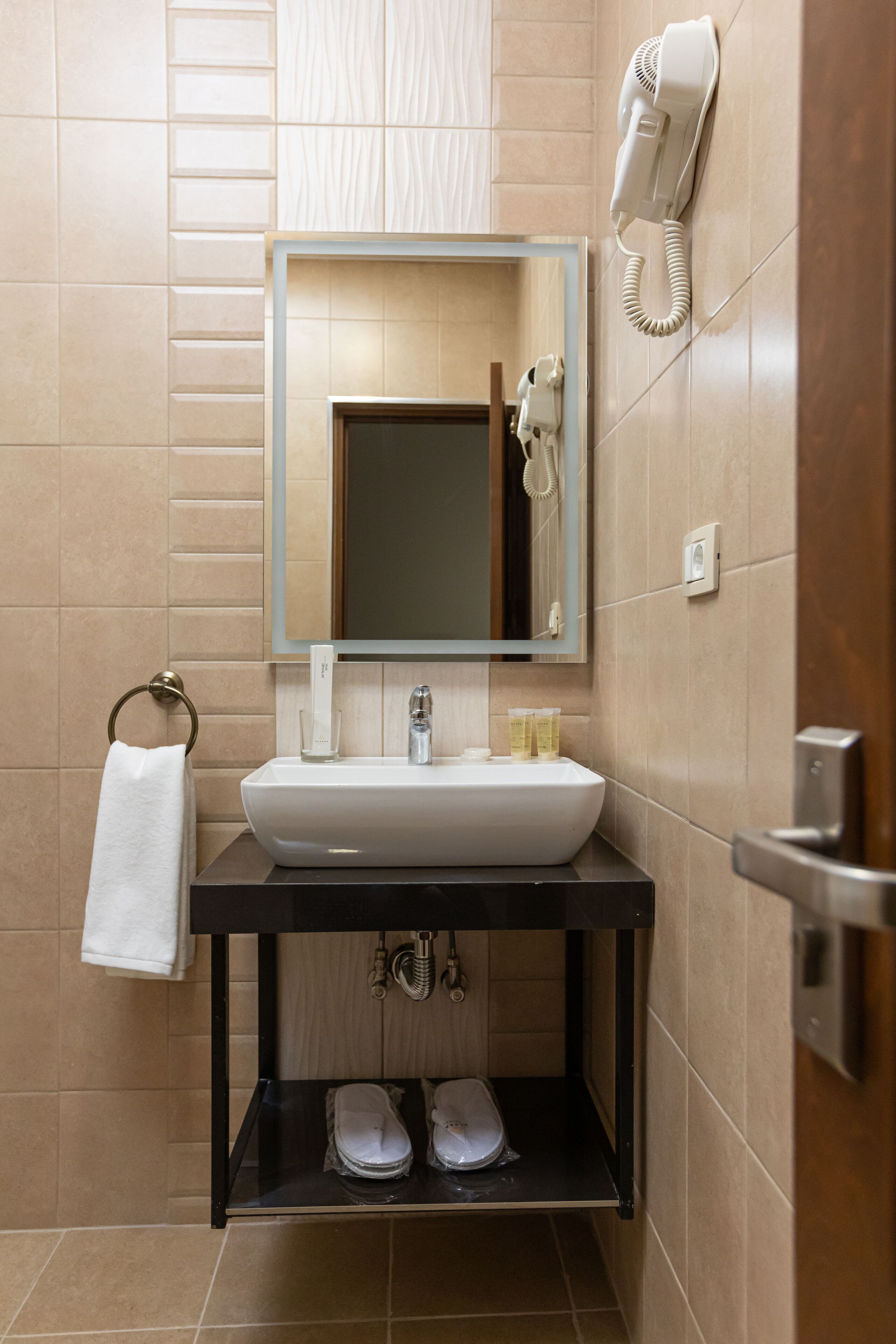 Une salle de bain équipée d’un lavabo, d’un miroir, d’un porte-serviettes et d’un sèche-cheveux fixé au mur.