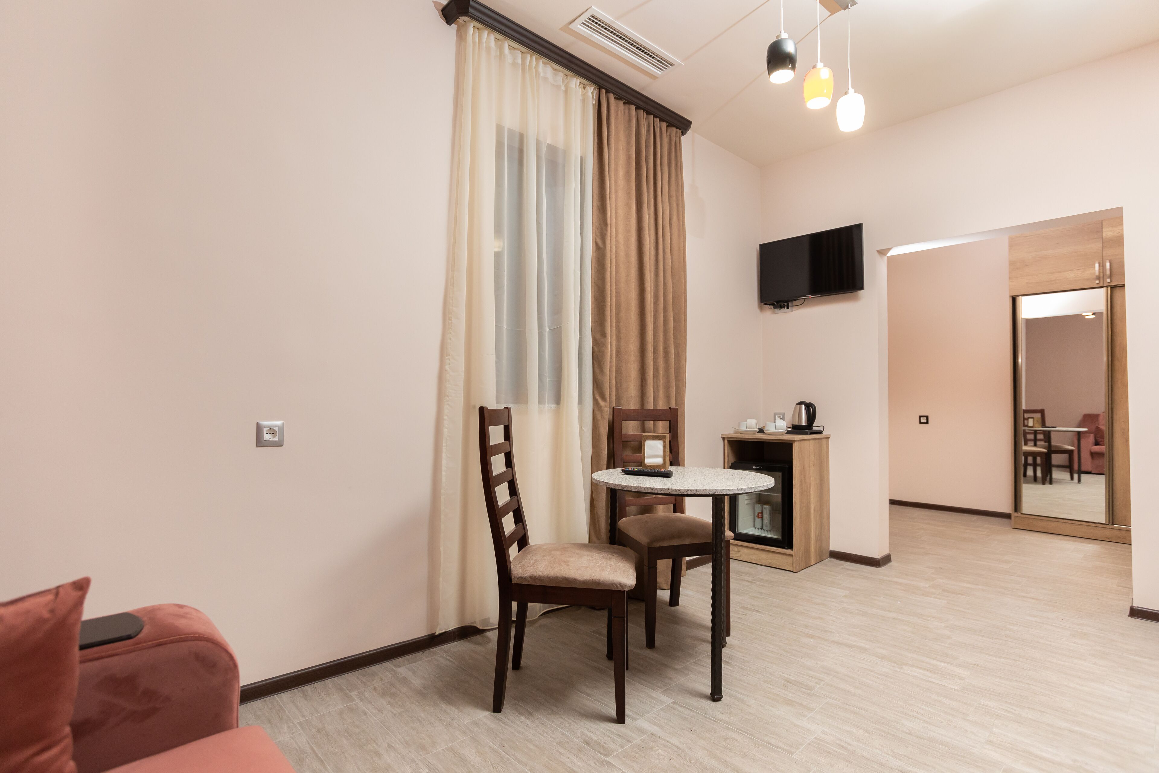 A hotel room with a dining area, a TV mounted on the wall, and a sliding door leading to another room.