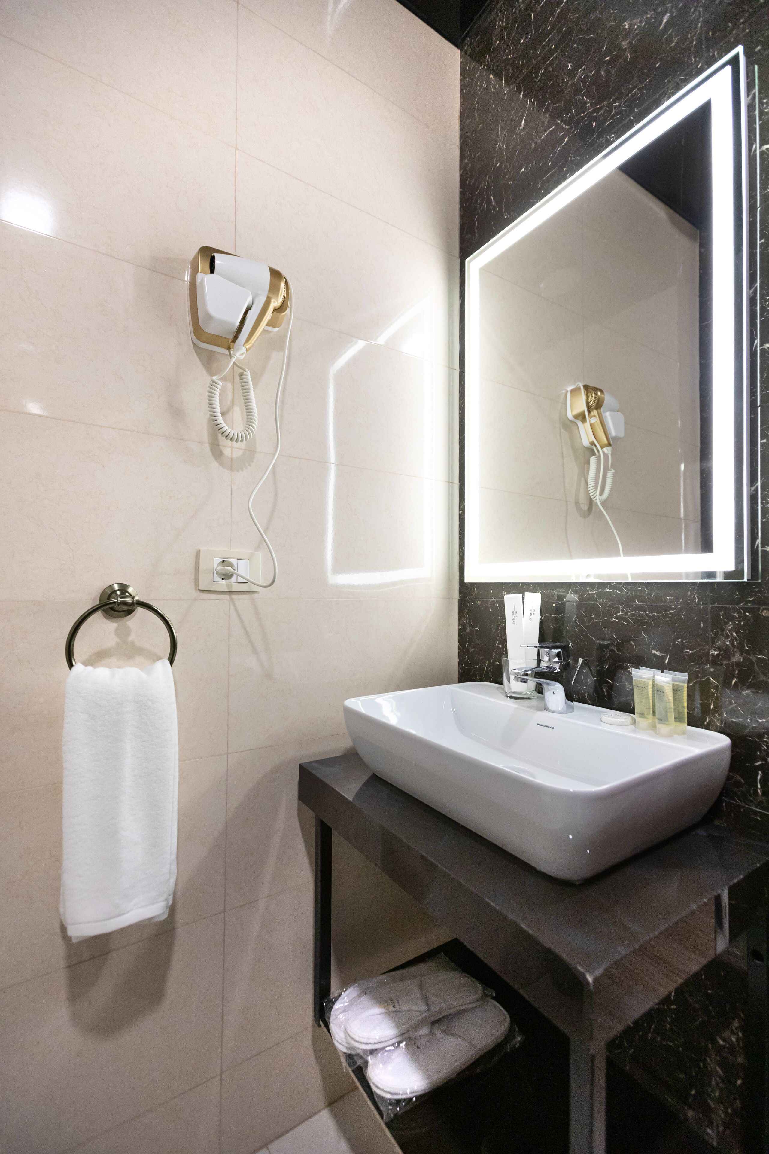 A modern bathroom with a large mirror, a sink, a towel ring, and a hairdryer mounted on the wall.