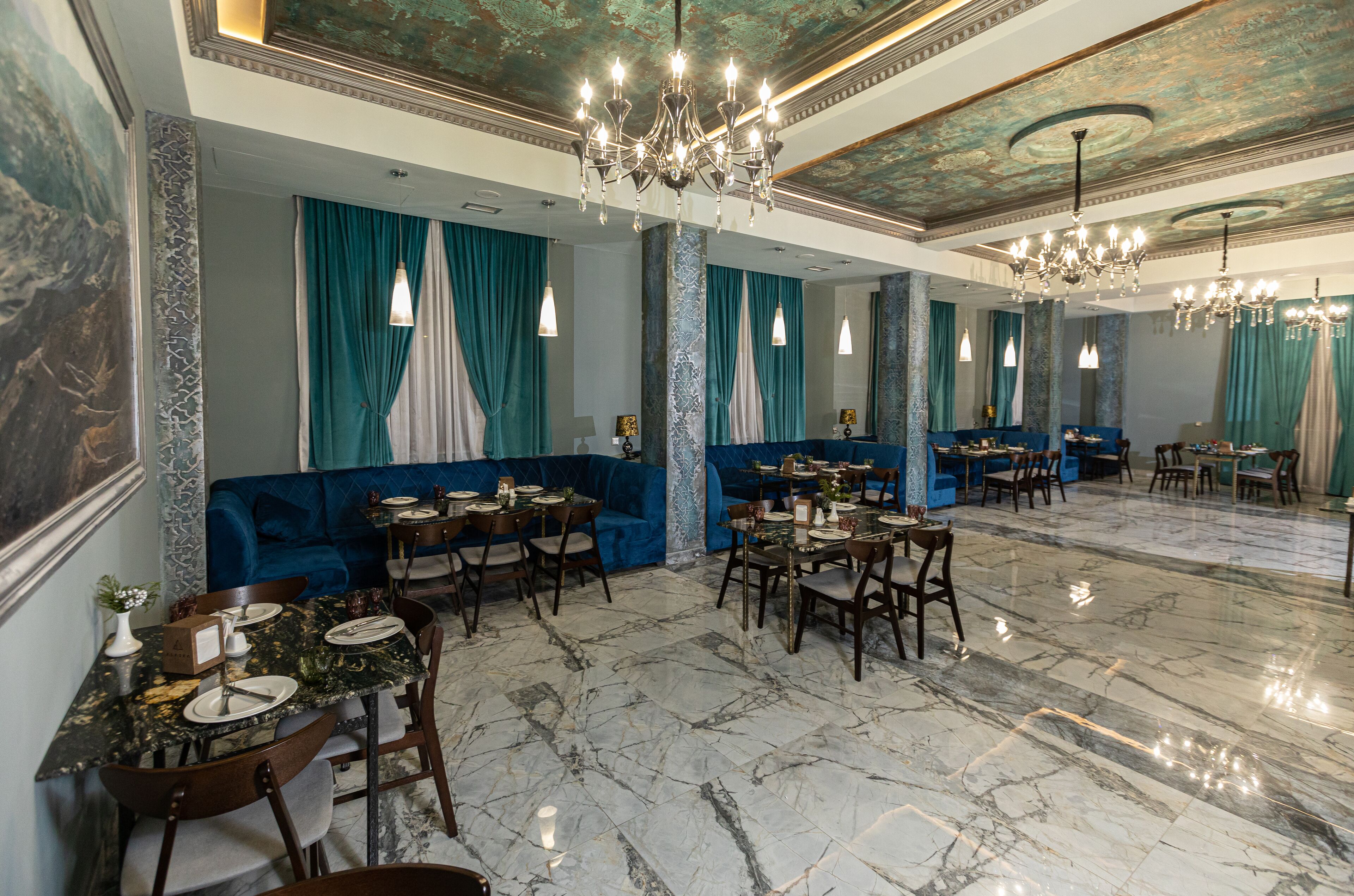 A spacious dining area with marble flooring, blue upholstered seating, and multiple chandeliers.