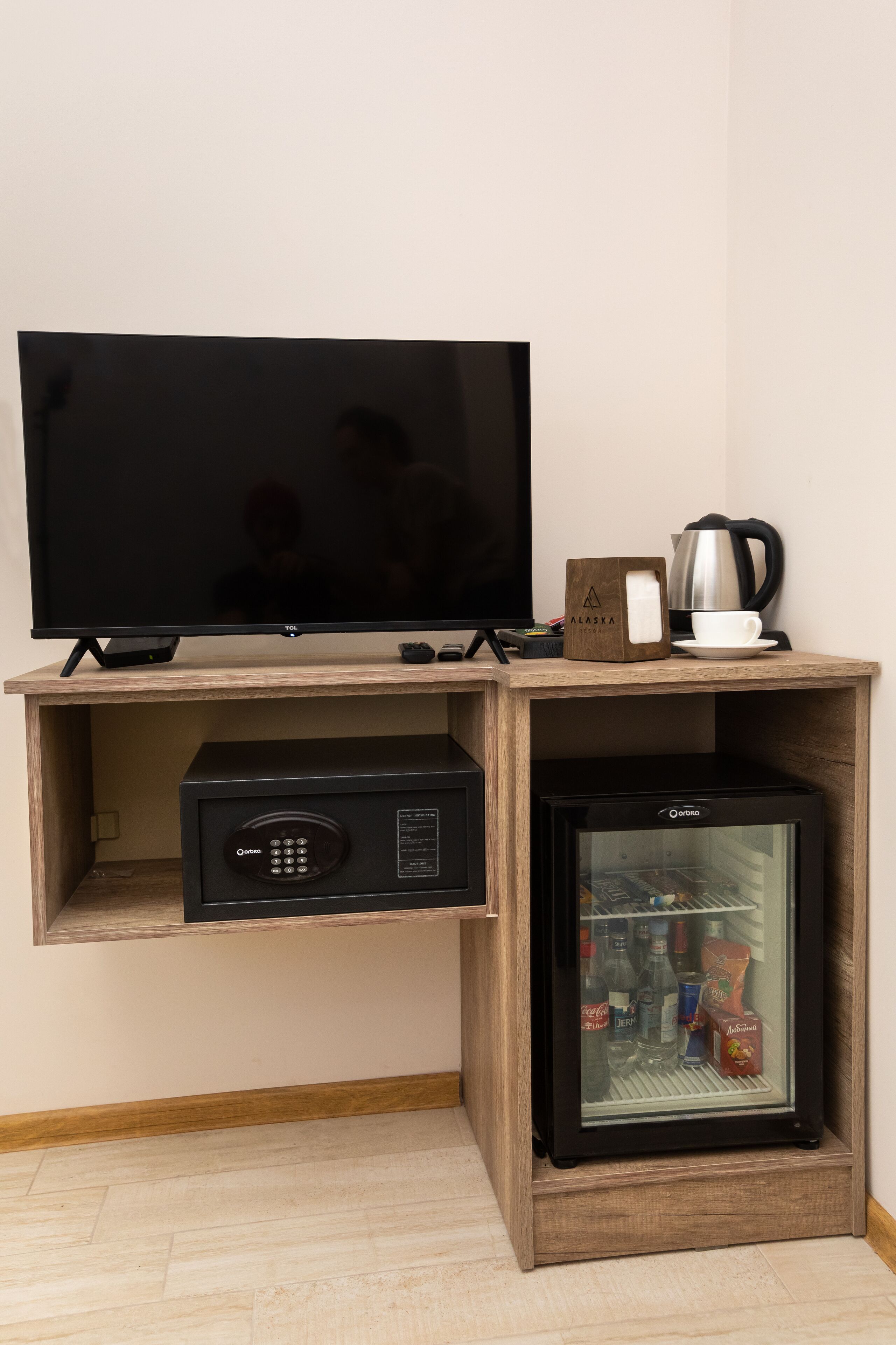 A television on a wooden shelf, a coffee maker, and a mini-fridge with beverages.