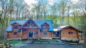 A log cabin with a metal roof, a porch, and a staircase leading to the entrance.
