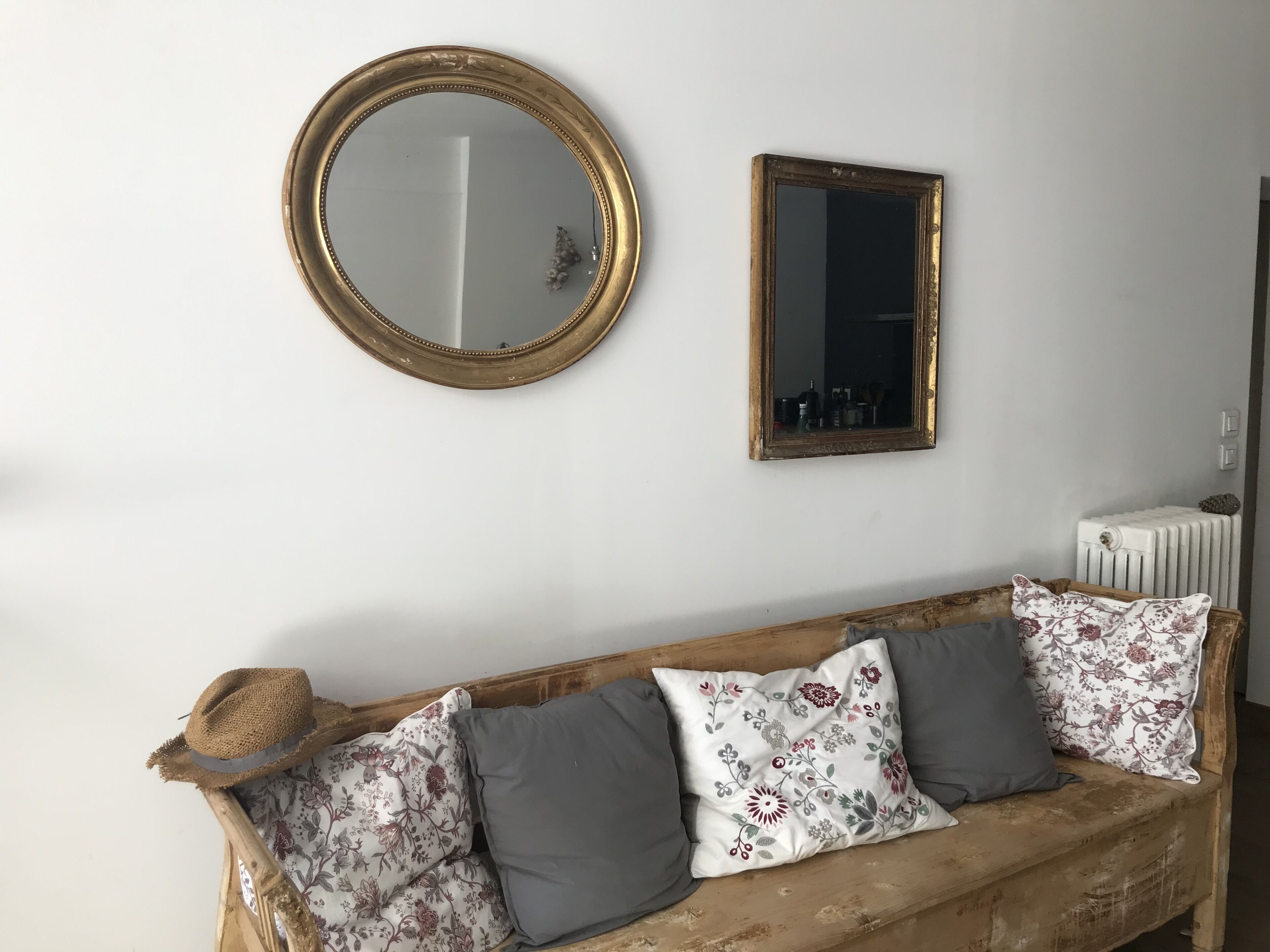 Una habitació amb un sofà de fusta, dos coixins, un mirall rodó i un mirall rectangular a la paret.