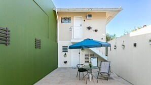 Een terras met een tafel, stoelen, een blauwe parasol en een trap naar een hoger gelegen niveau.