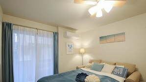 Un dormitorio con cama, ventilador de techo, ventana con cortinas, aire acondicionado de pared y lámpara de noche.