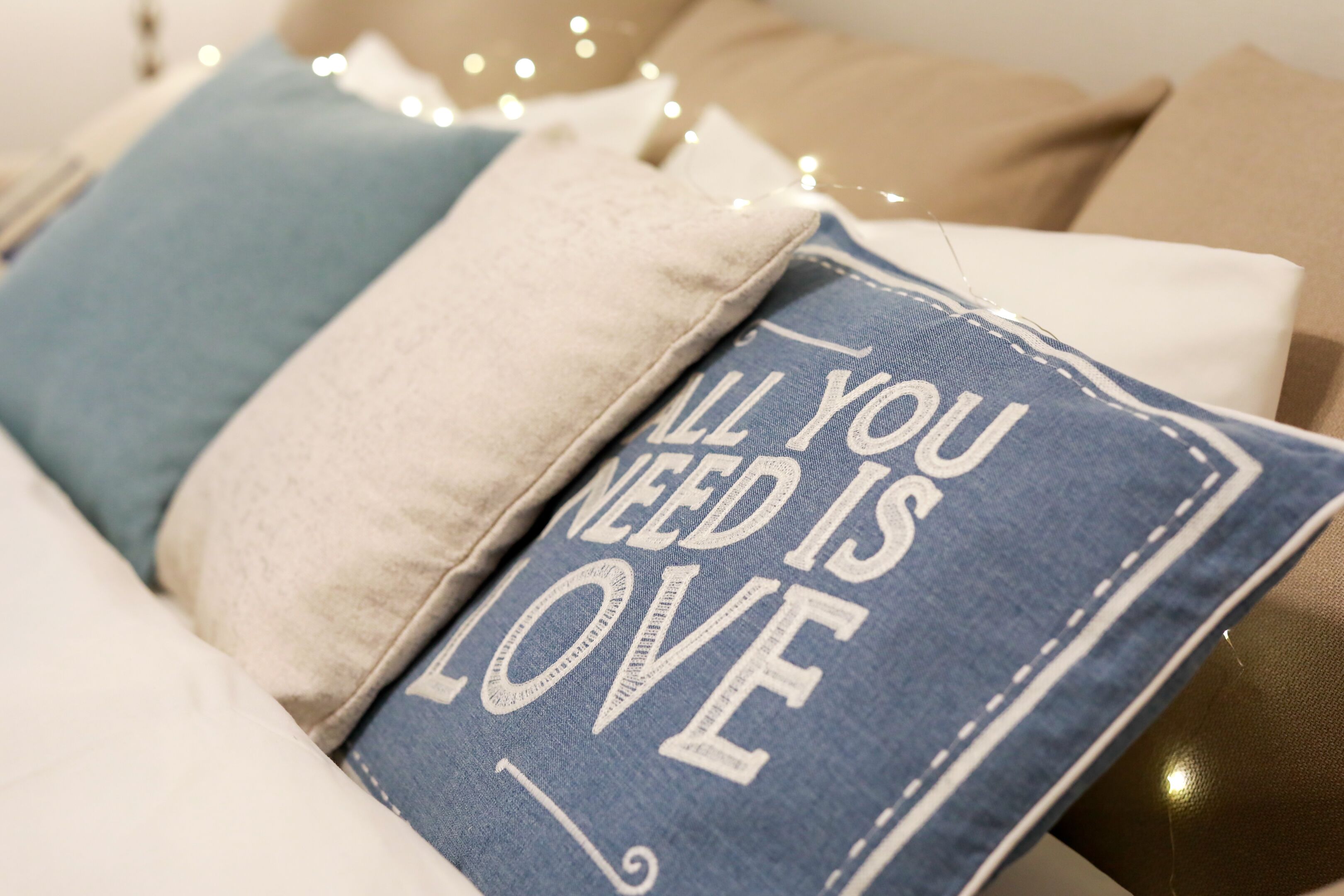 Ein Nahaufnahme eines Kussens mit dem Aufdruck 'ALL YOU NEED IS LOVE' auf blauem Stoff.