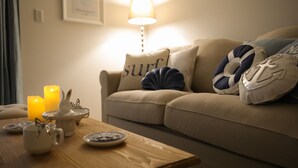 Una sala de estar acogedora con un sofá color beige, cojines decorativos, una mesa de centro de madera y una vela encendida.