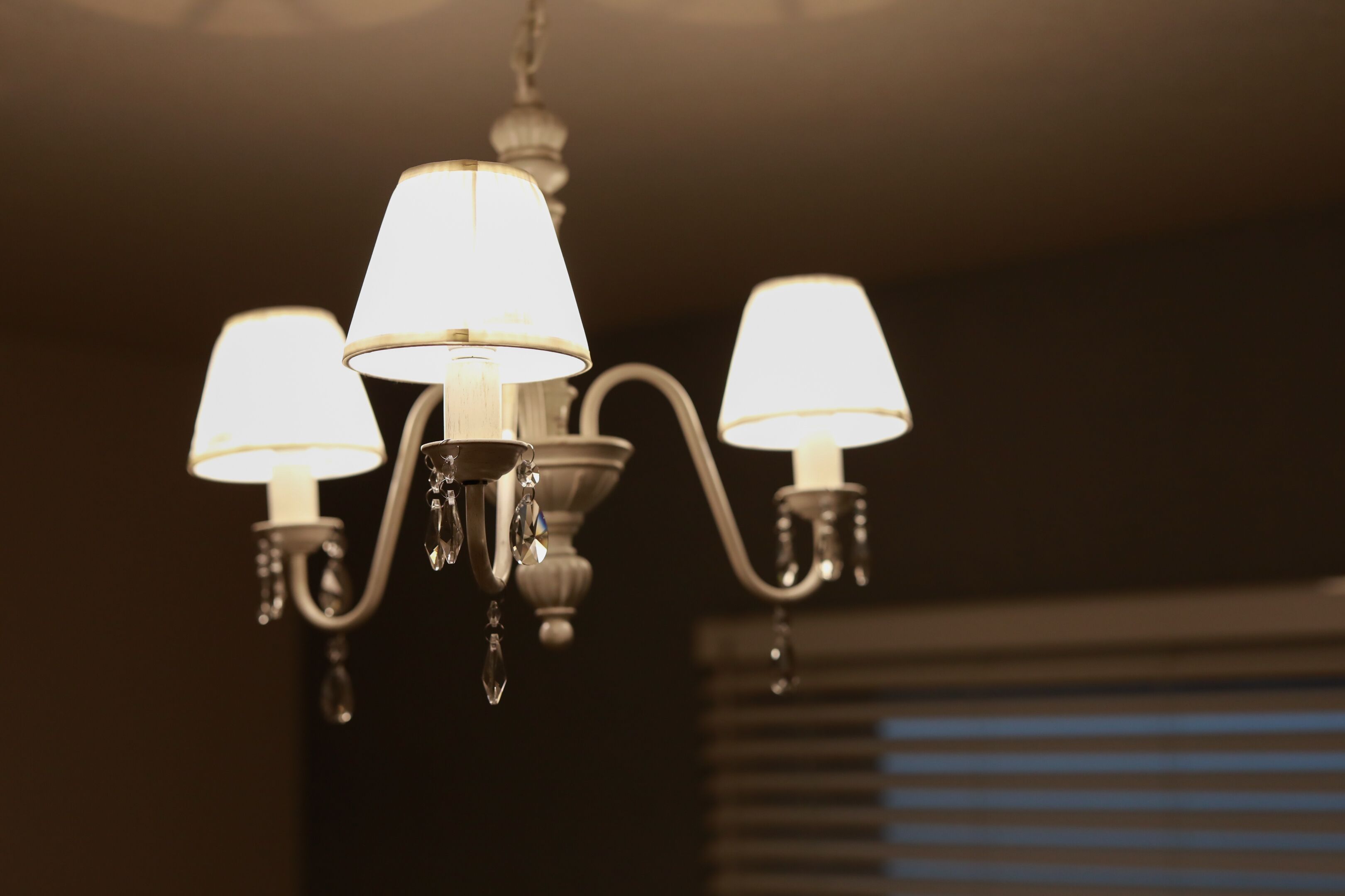 A chandelier with three lampshades in a dimly lit room.