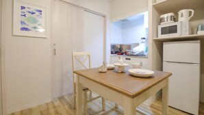 Una cocina pequeña con una mesa de madera, armarios blancos y un refrigerador.