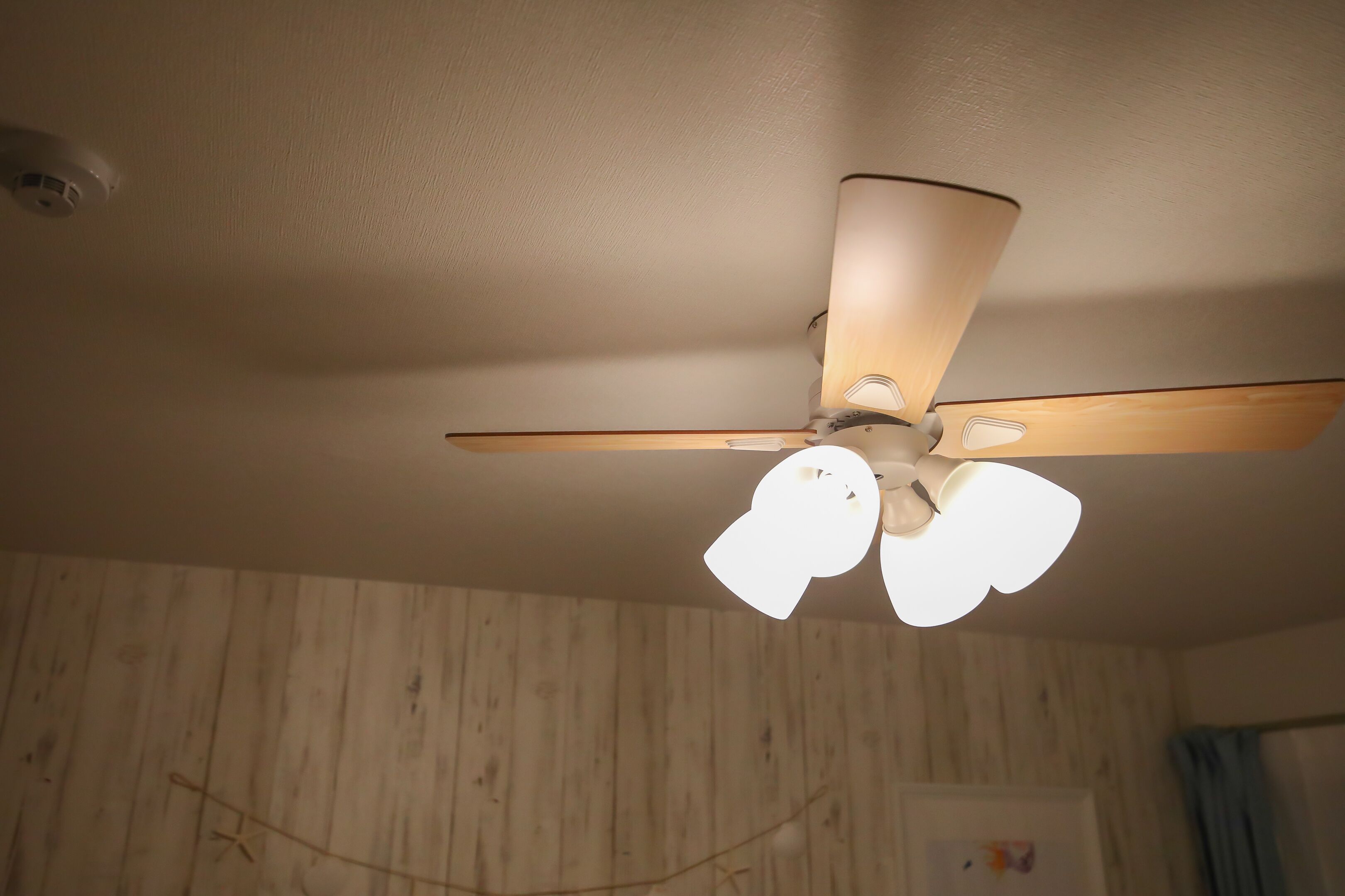 Un ventilador de techo con tres lámparas en una habitación con paneles de madera.