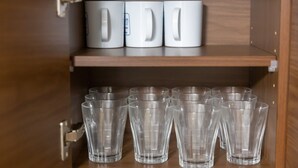 Ett träskåp med tre vita muggar på den övre hyllan och flera genomskinliga glas på den nedre hyllan.