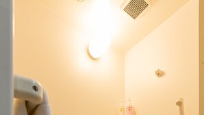 Ett litet, väl upplyst badrum med dusch, handduksställ och en hylla med toalettartiklar.