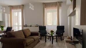 A living room with a brown sofa, two black chairs, a coffee table, and a TV. - Large Three-room Apartment in a Strategic Position (Desenzano del Garda)