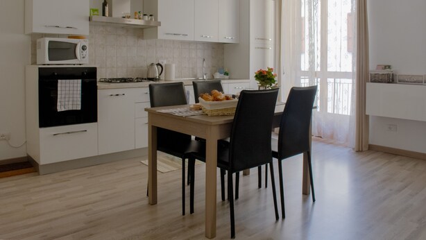 A modern kitchen with white cabinets, a microwave, a gas stove, and a dining area with a table and chairs. - Large Three-room Apartment in a Strategic Position (Desenzano del Garda)