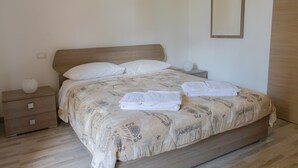 A neatly made bed with a patterned bedspread, a bedside table with a vase, and a mirror on the wall. - Large Three-room Apartment in a Strategic Position (Desenzano del Garda)