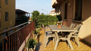 A balcony with a table and chairs, surrounded by potted plants and a view of neighboring buildings. - Large Three-room Apartment in a Strategic Position (Desenzano del Garda)