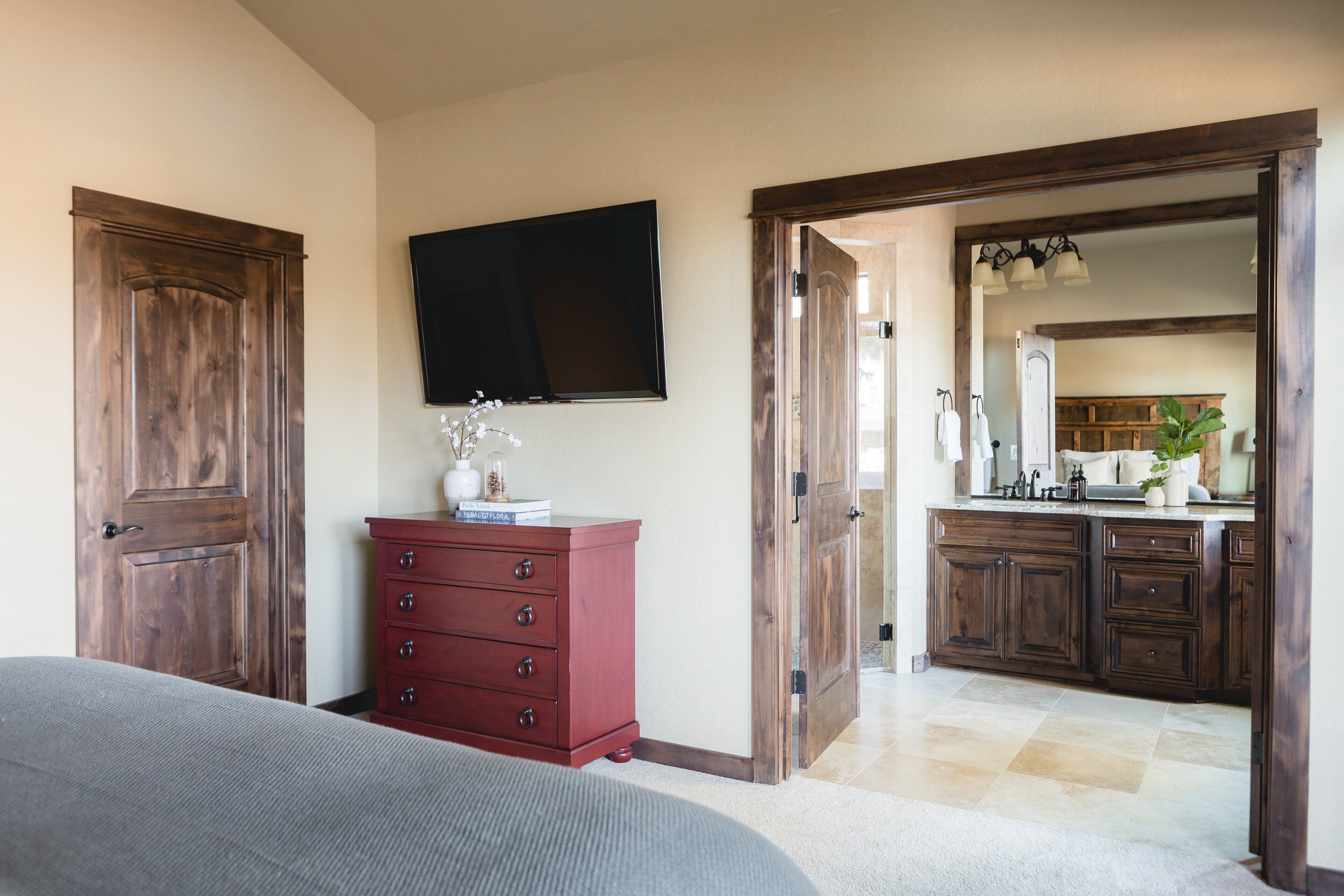 Une chambre à coucher avec un grand lit, une armoire en bois, une commode et un téléviseur à écran plat fixé au mur.