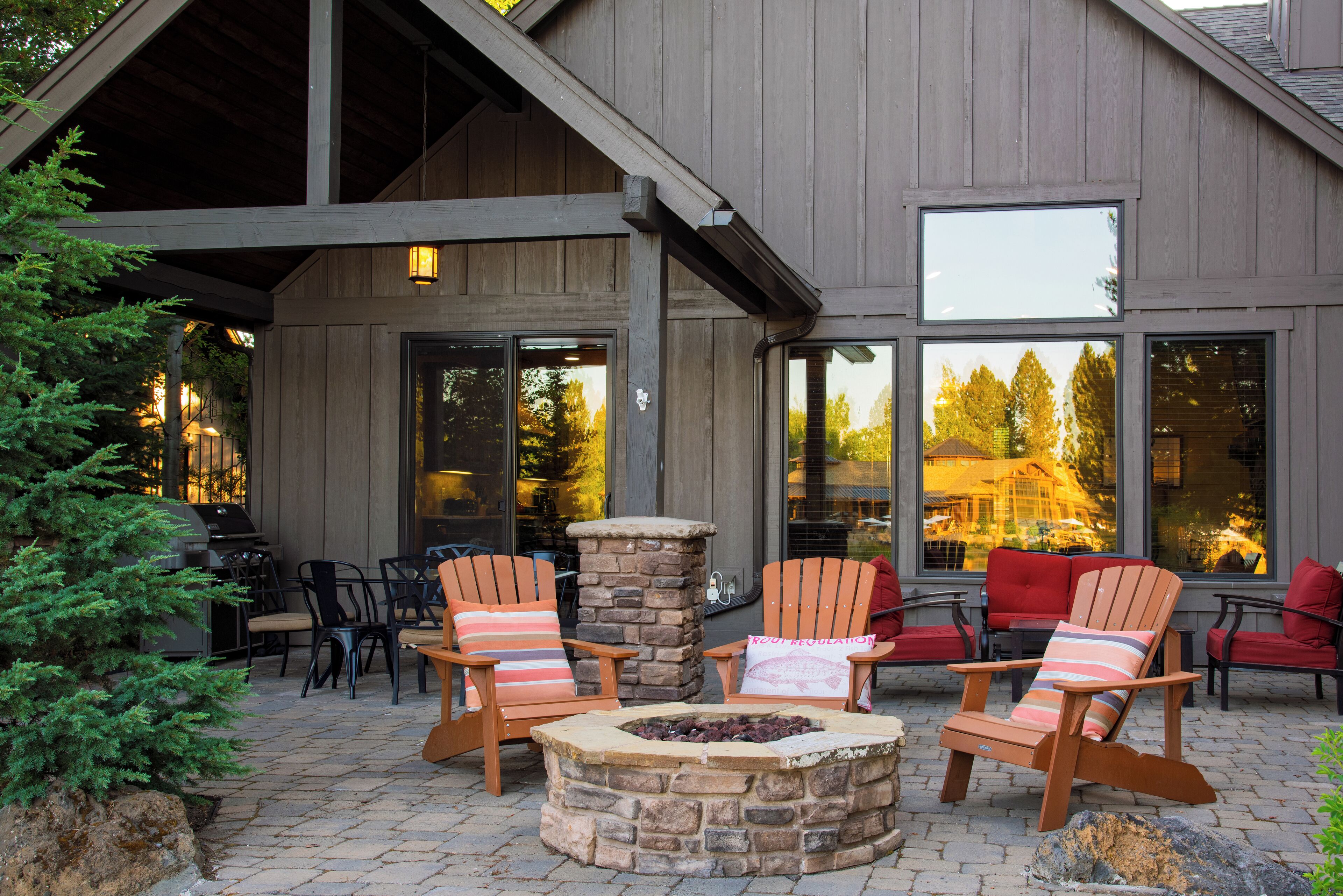 An outdoor patio with stone fire pit, wooden Adirondack chairs, and a stone chimney.