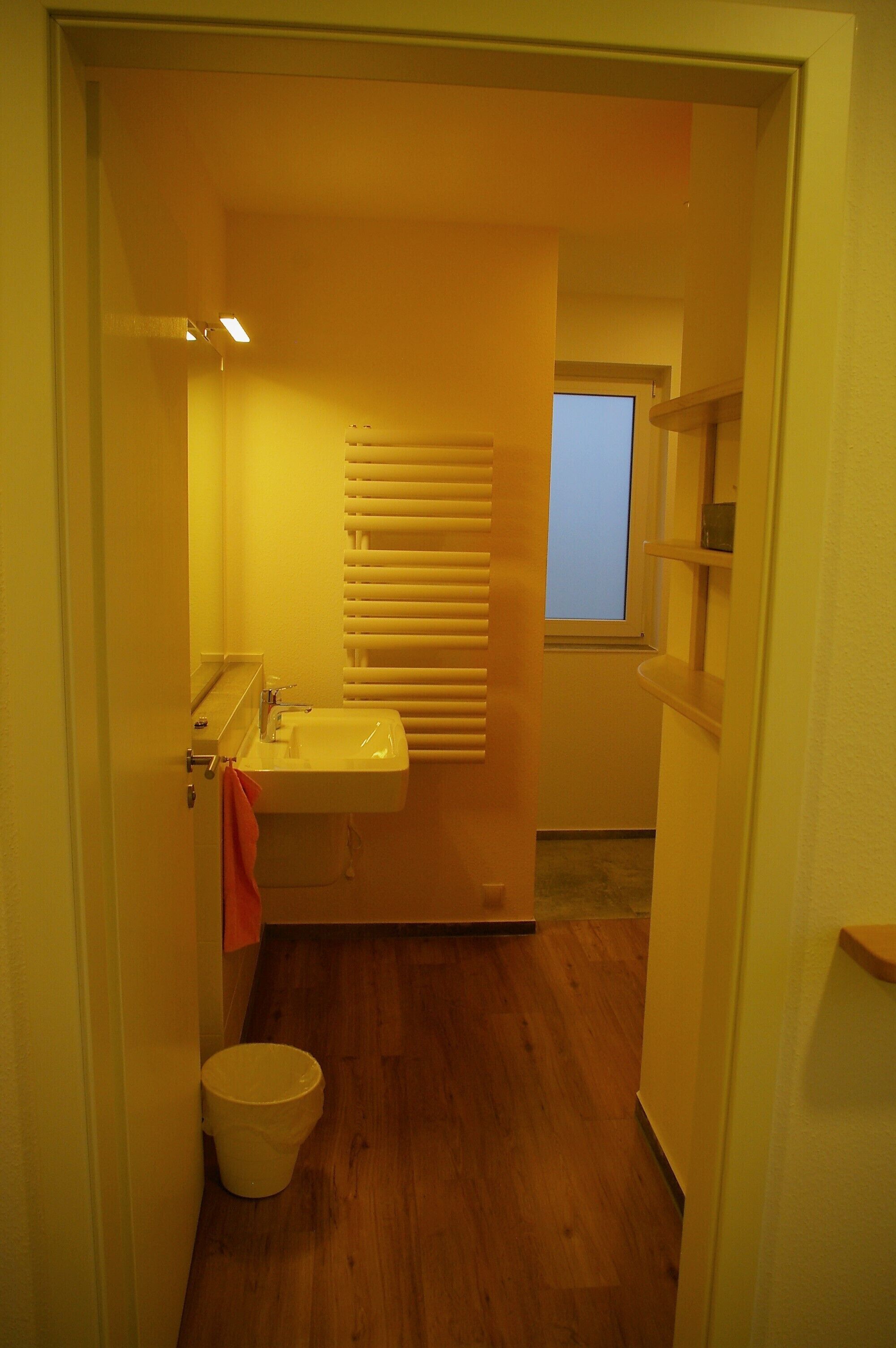 A narrow bathroom with a sink, a window, and a wooden floor.