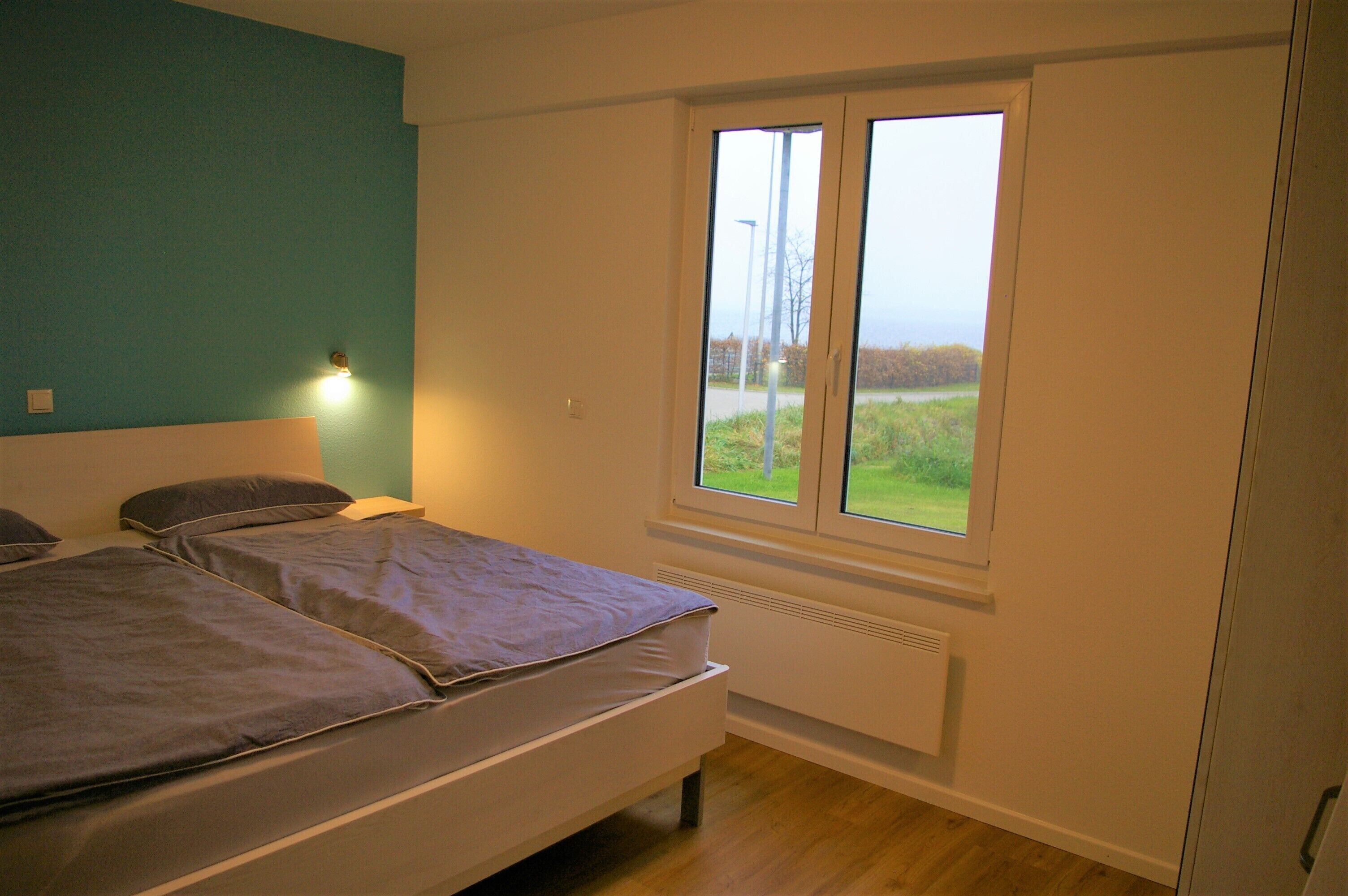 Une chambre avec deux lits, une fenêtre donnant sur l’extérieur et un luminaire fixé au mur.