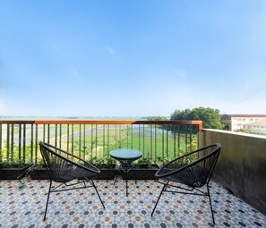 A balcony with two black wire chairs and a small round table, overlooking a green field and a building in the distance. - Paddy Boutique House Hoian (Da Nang)
