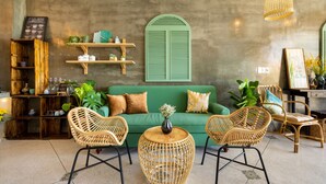 Een gezellige zithoek met een groene bank, rieten stoelen, een houten salontafel en een hanglamp.