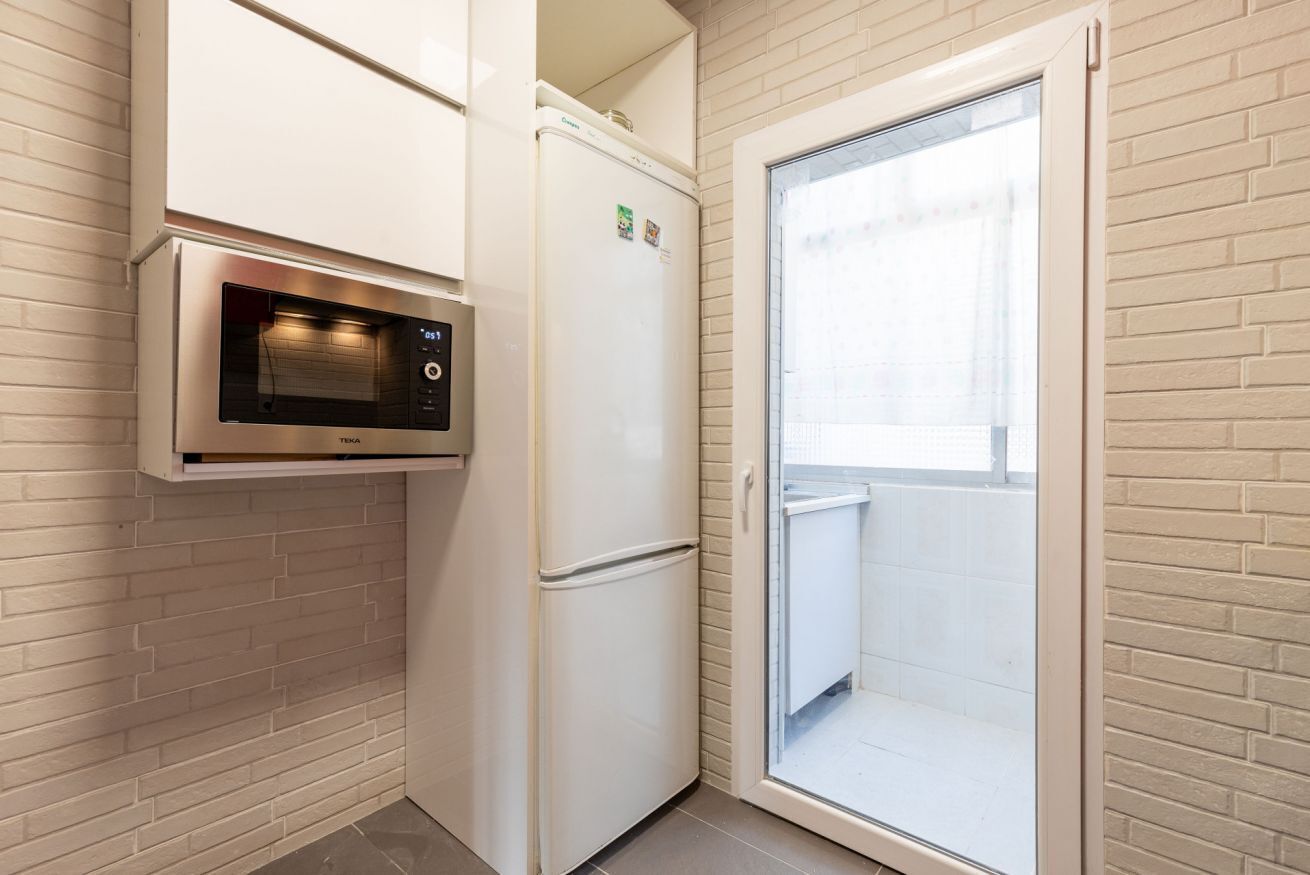 A compact kitchen with a microwave, refrigerator, and a sliding glass door leading to a balcony.