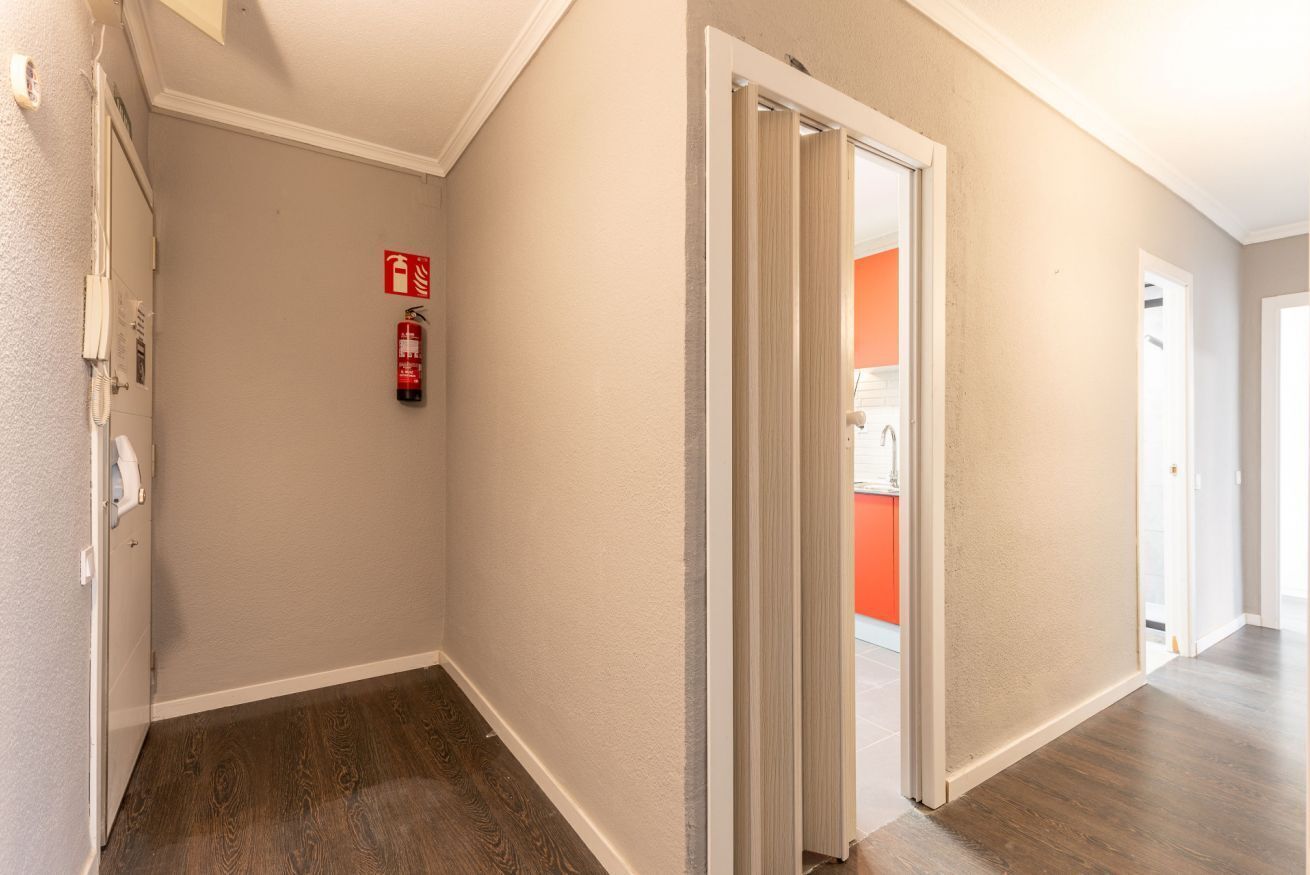 A hallway with a fire extinguisher, a door leading to a room with an orange wall, and a white door at the end.